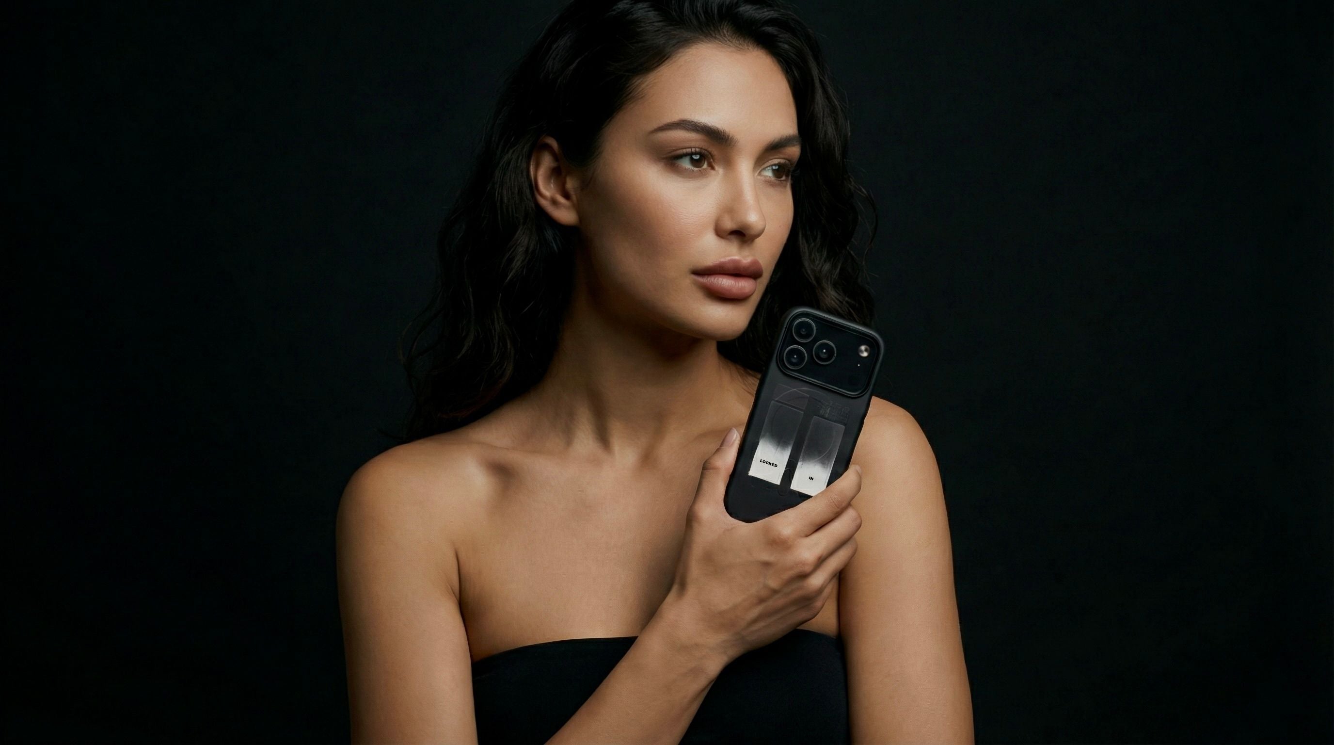 A woman in a photoshoot on a black background, holding an iPhone with Aesmor case